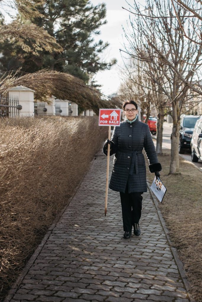 Real estate agent walking on a path, holding a For Sale sign.