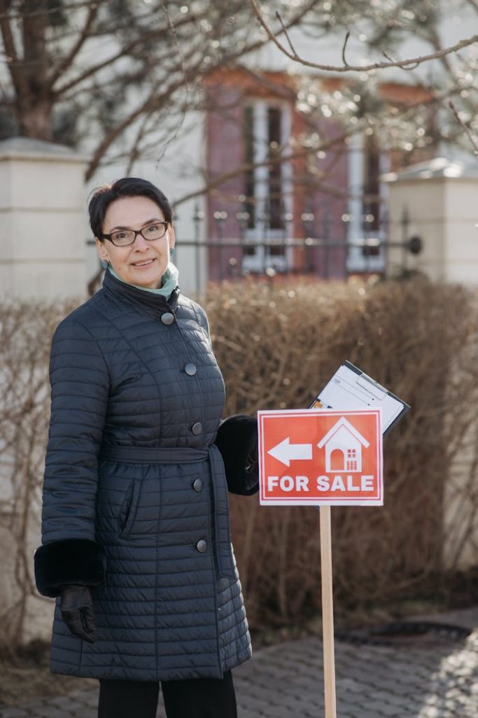 Realtor posing with a for sale sign outside a house, showcasing real estate services.