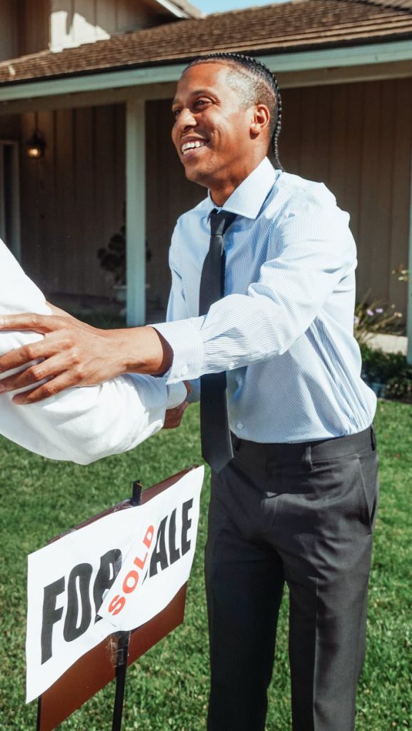 Man shaking hands outside a house with a Sold sign, marking a successful real estate transaction.