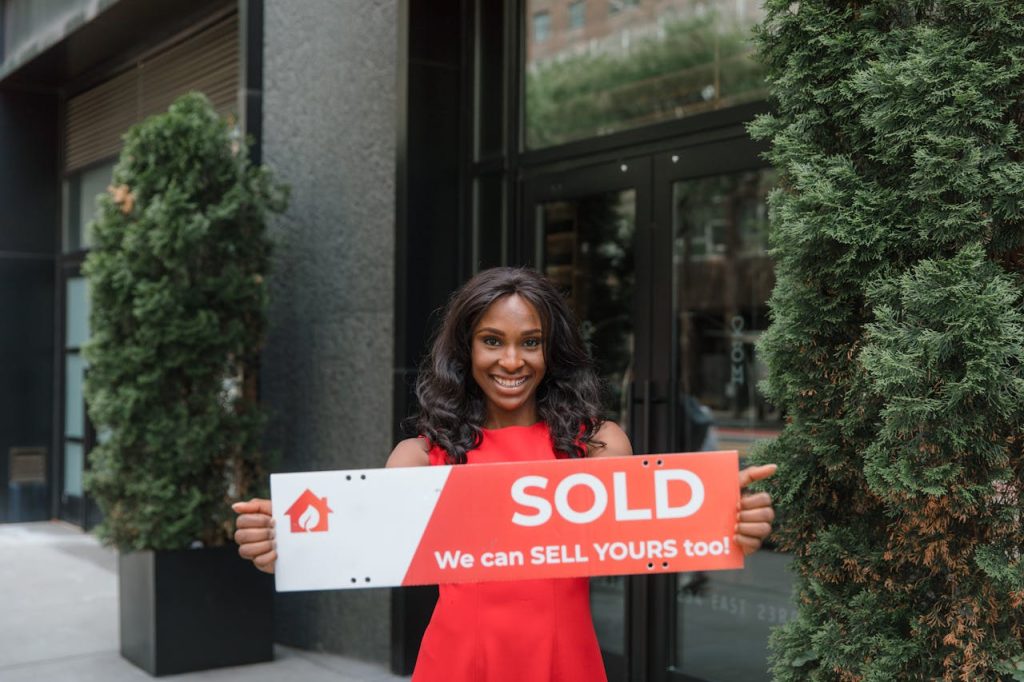 Confident real estate agent holds SOLD sign in front of building, symbolizing success.