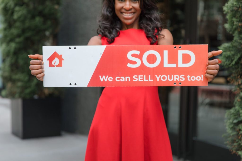 Smiling woman holding a Sold sign, symbolizing successful real estate sales.