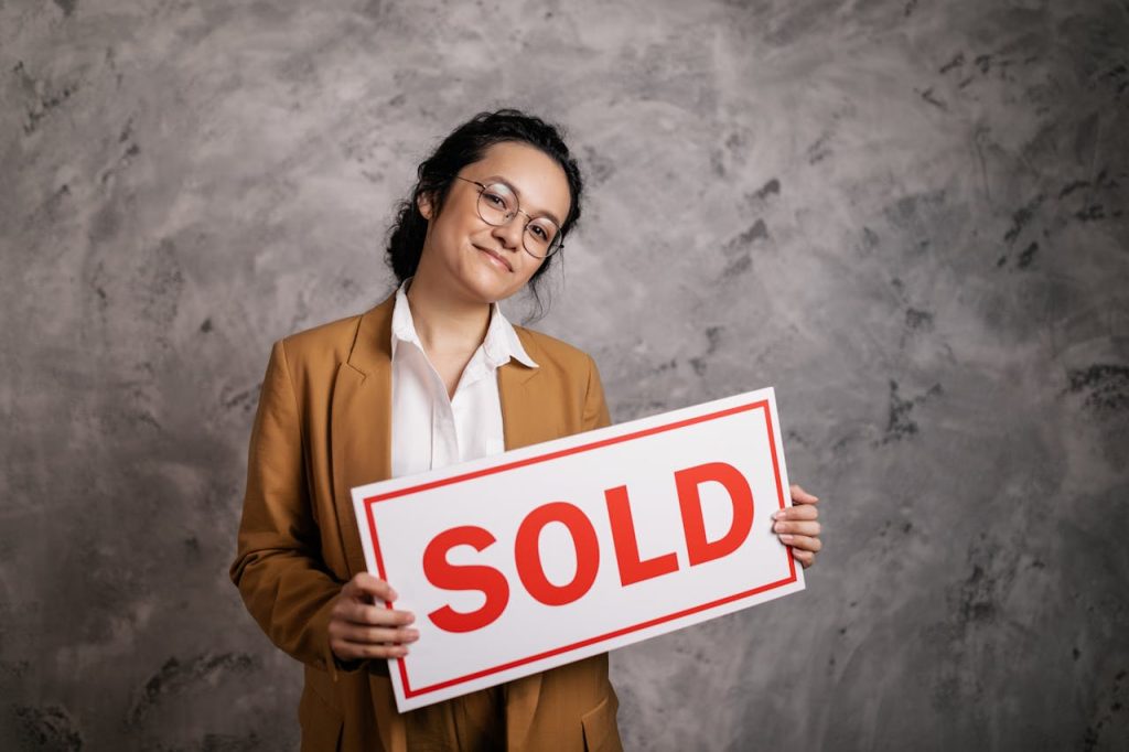 Confident real estate agent holding a Sold sign indoors, symbolizing successful property sale.
